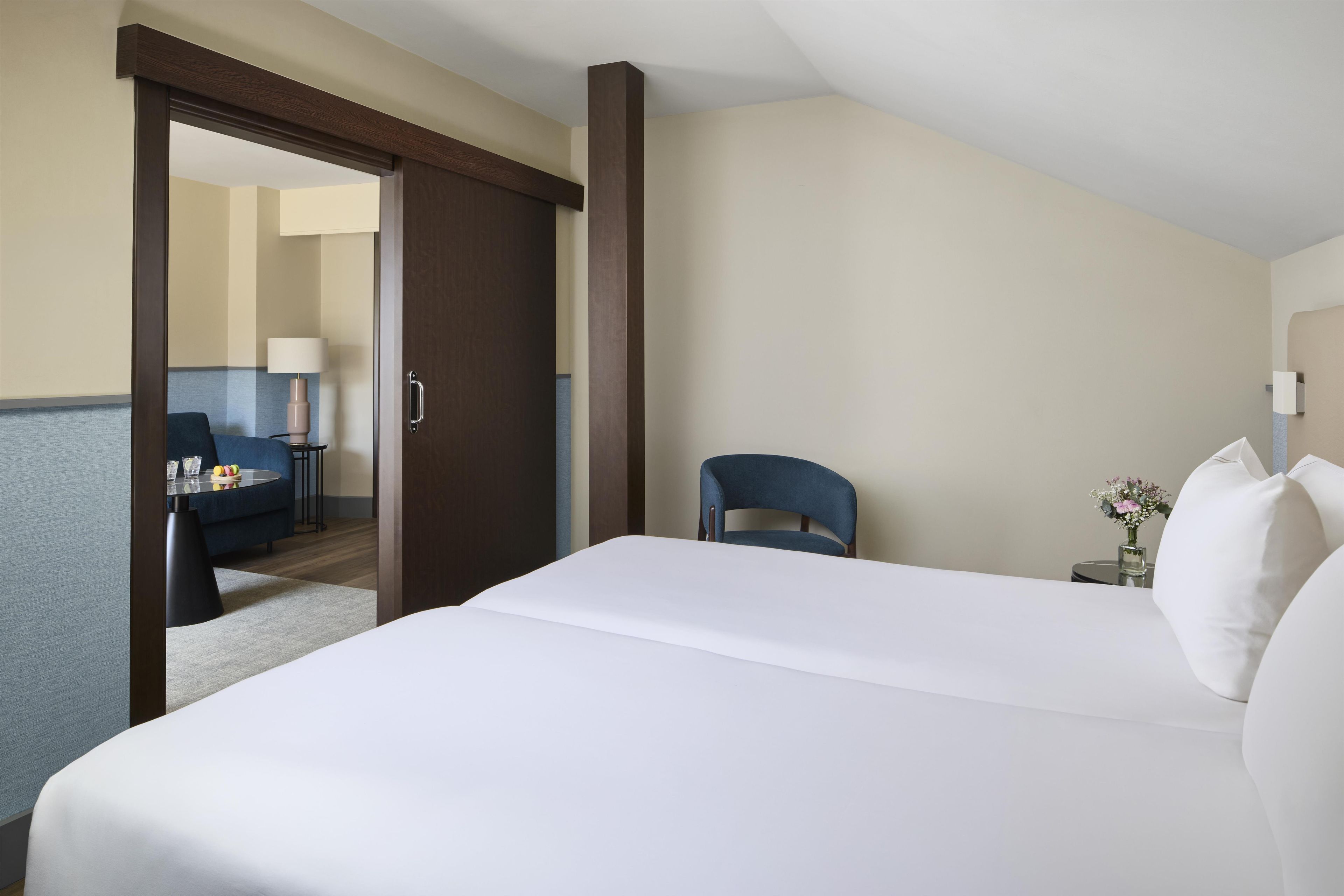 A hotel room with a bed, a chair, a desk, and a lamp.