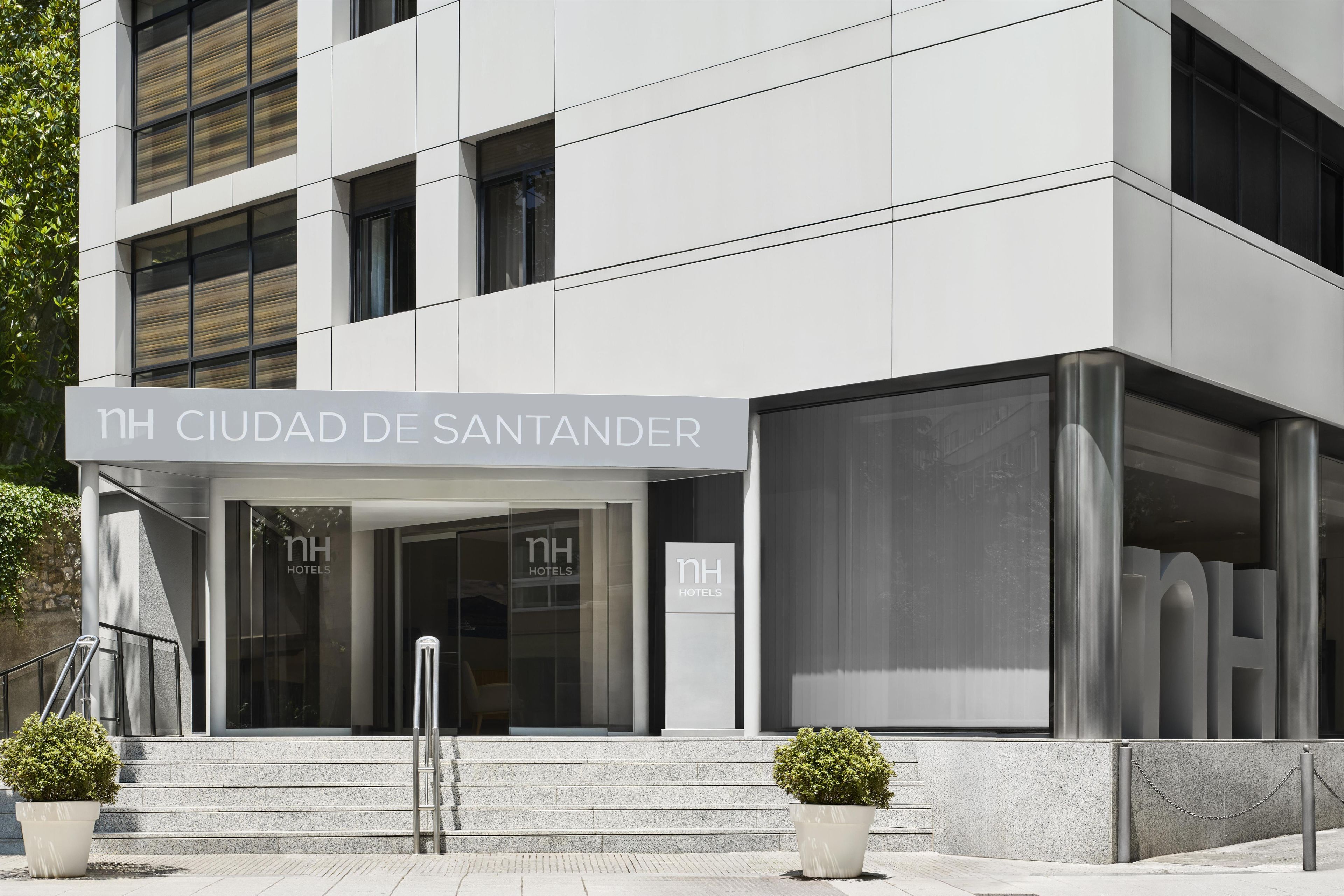 Una entrada moderna de hotel con un cartel que dice 'NH CIUDAD DE SANTANDER' y 'NH HOTELS' en las puertas de cristal.