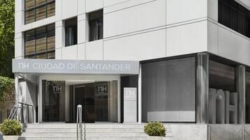 Een moderne hotelentree met een bord waarop 'NH CIUDAD DE SANTANDER' en 'NH HOTELS' op de glazen deuren staat.