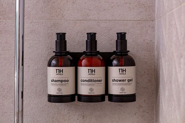 Three bottles of hotel toiletries (shampoo, conditioner, shower gel) on a wall. - NH Ciudad de Santander (Santander)