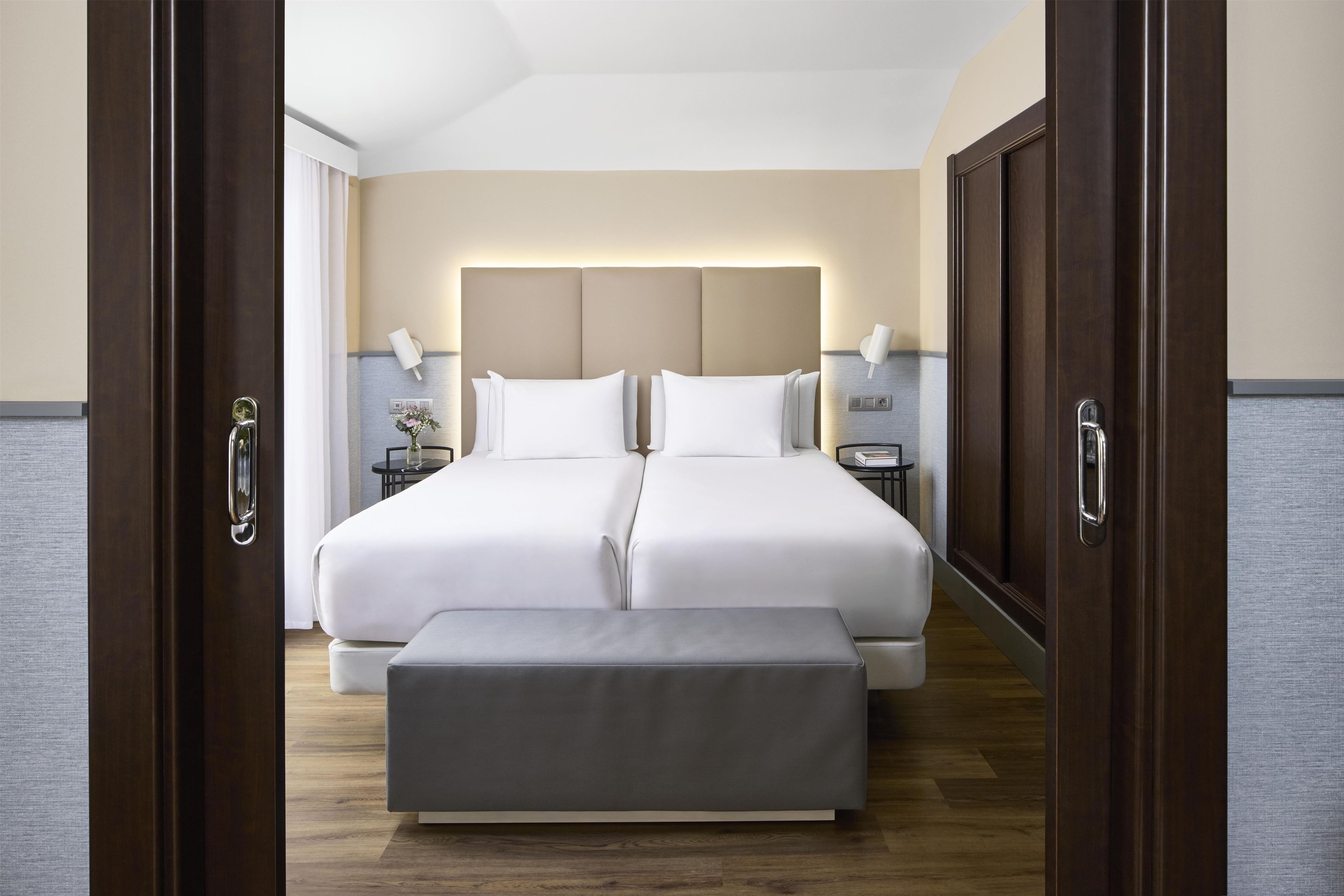 Cama doble con cabecera, mesitas de noche y un banco en una habitación de hotel.