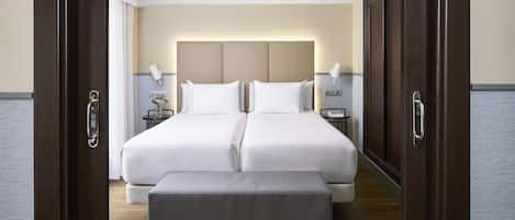 A double bed with a headboard, bedside tables, and a bench in a hotel room.