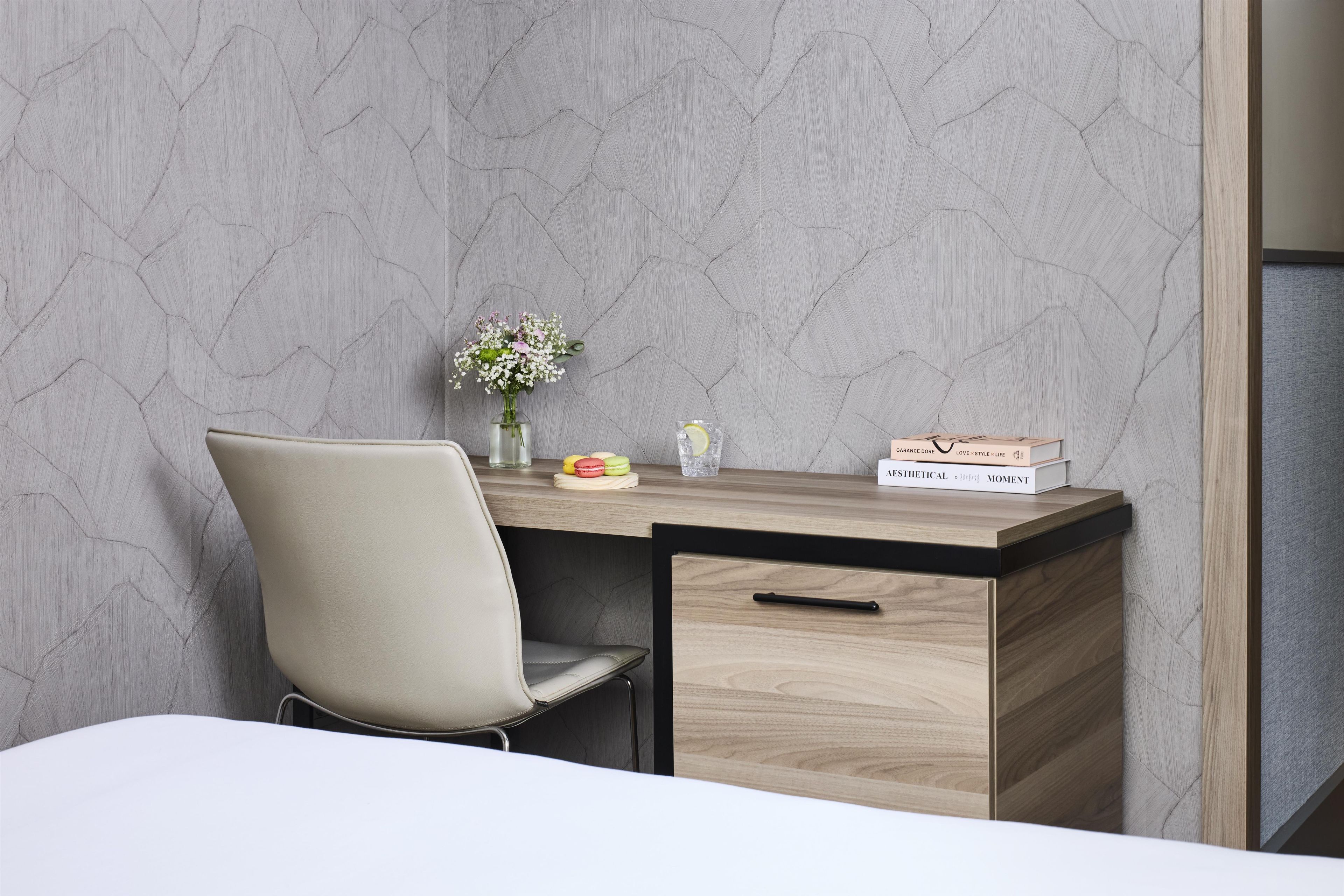A modern desk with a vase of flowers, a glass of water, and a box of macarons.