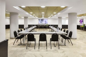 Un salón de conferencias con una larga mesa, sillas y una pantalla grande al frente.