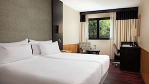 Una habitación de hotel con dos camas, un escritorio, una silla, un ventanal con cortinas y una lámpara.
