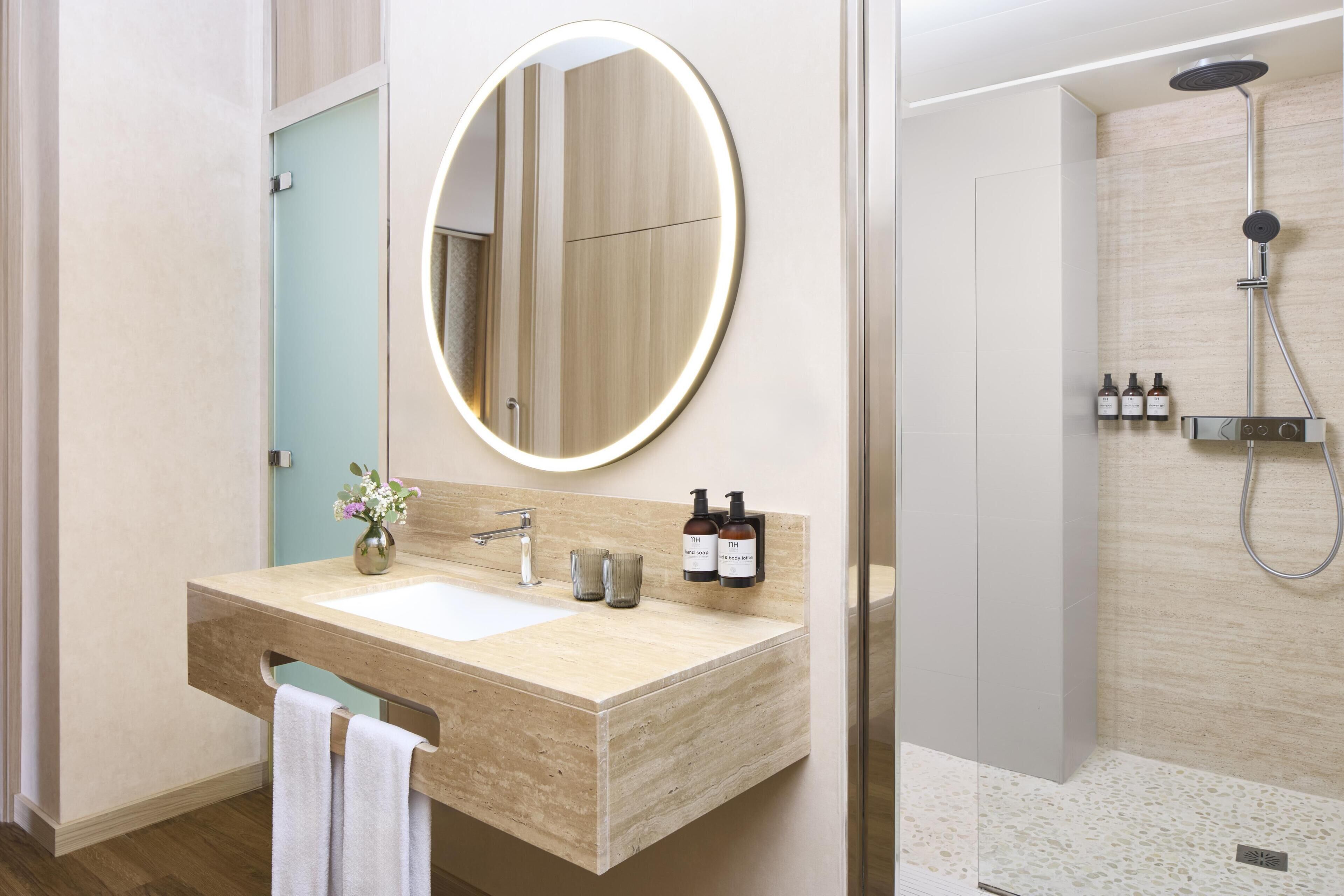 A modern bathroom with a wooden vanity, a round mirror, a shower, and a towel rack.