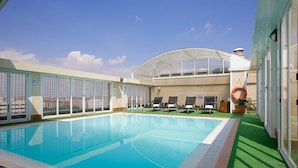 Una piscina en la azotea con cerramiento de vidrio, sillas de descanso y vistas de la ciudad.