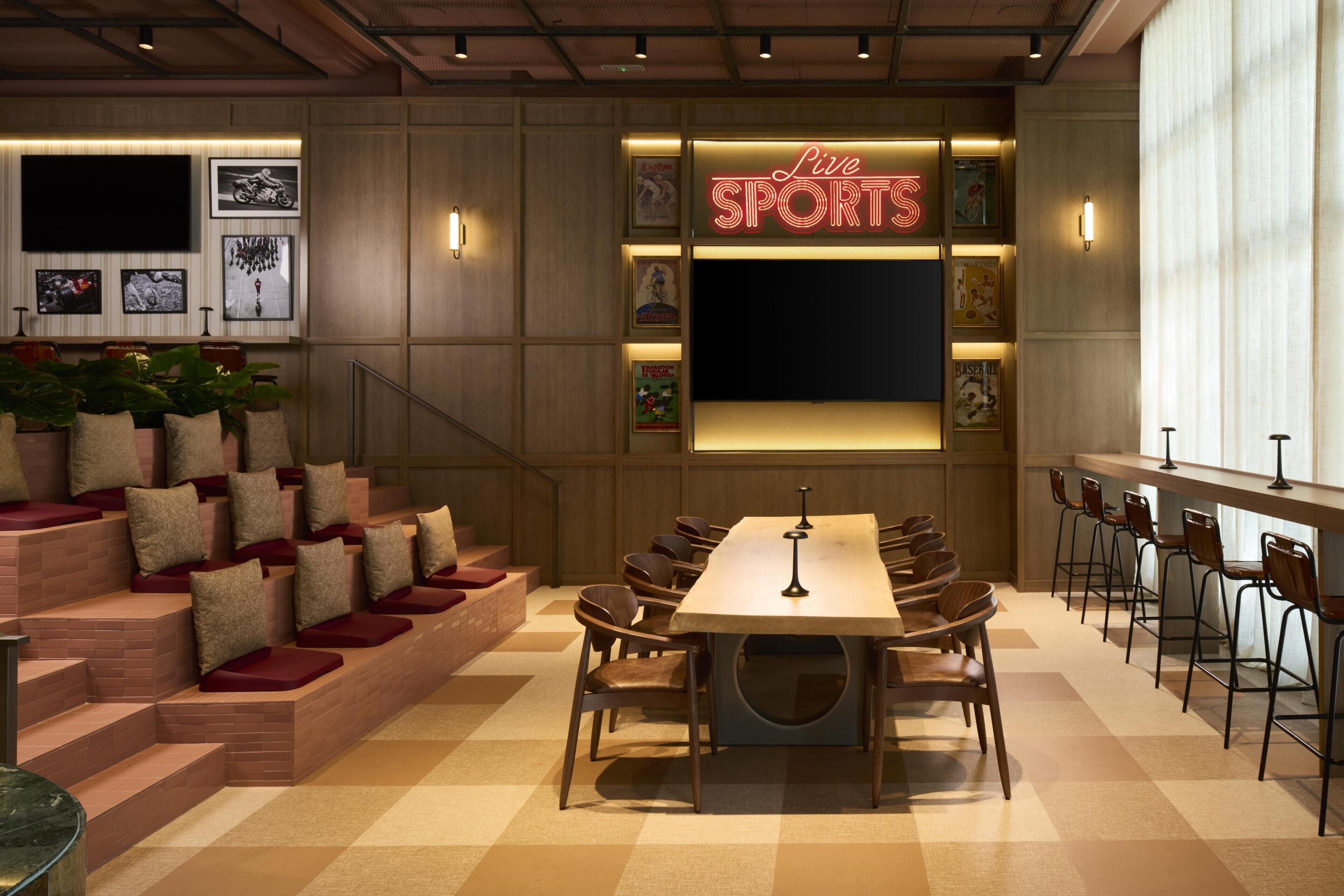 Een restaurant met een lange tafel, stoelen, een neonbord en ingelijste foto's aan de muur.
