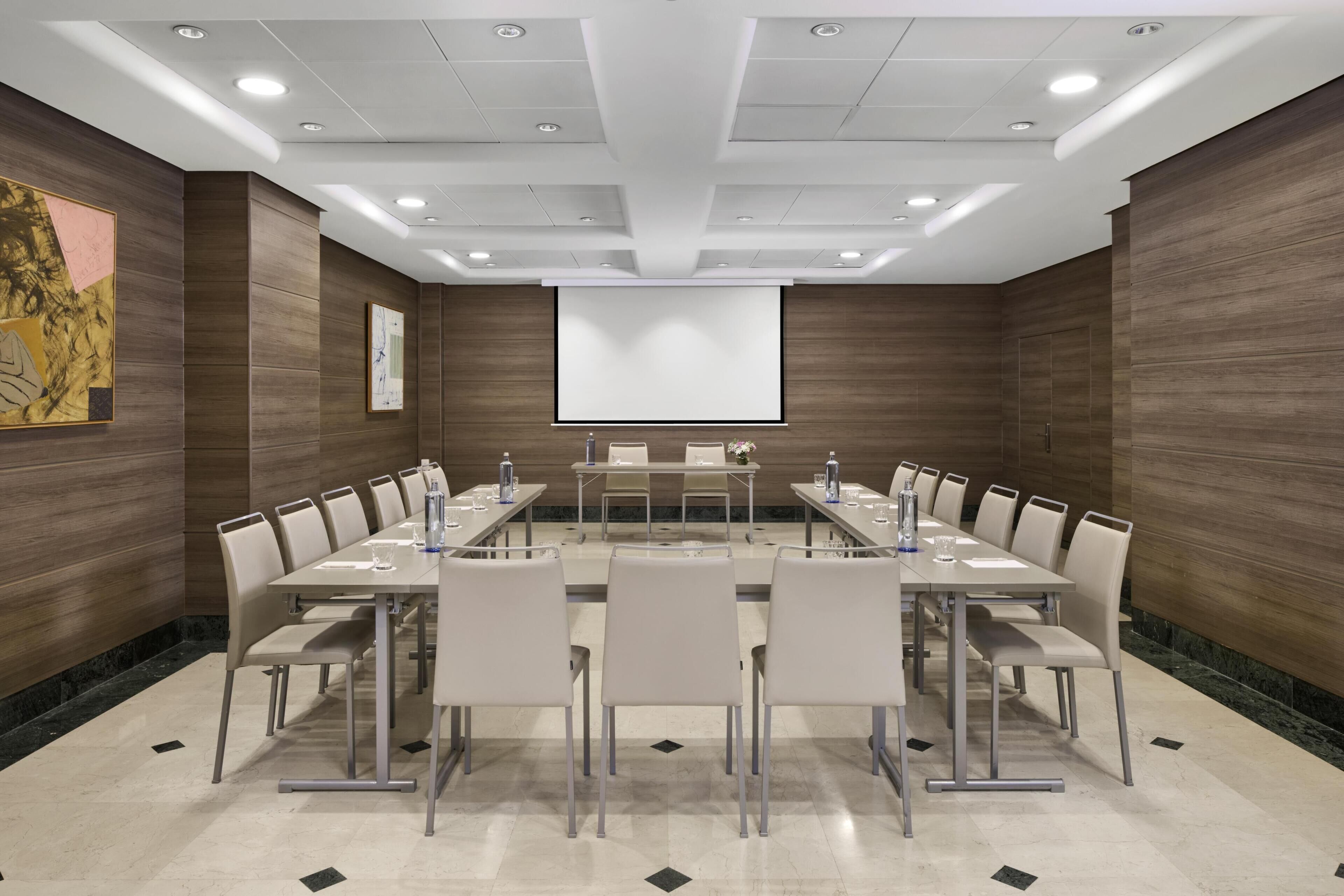 Une salle de conférence équipée d’une longue table, de chaises, d’un écran de projection et d’un tableau blanc.