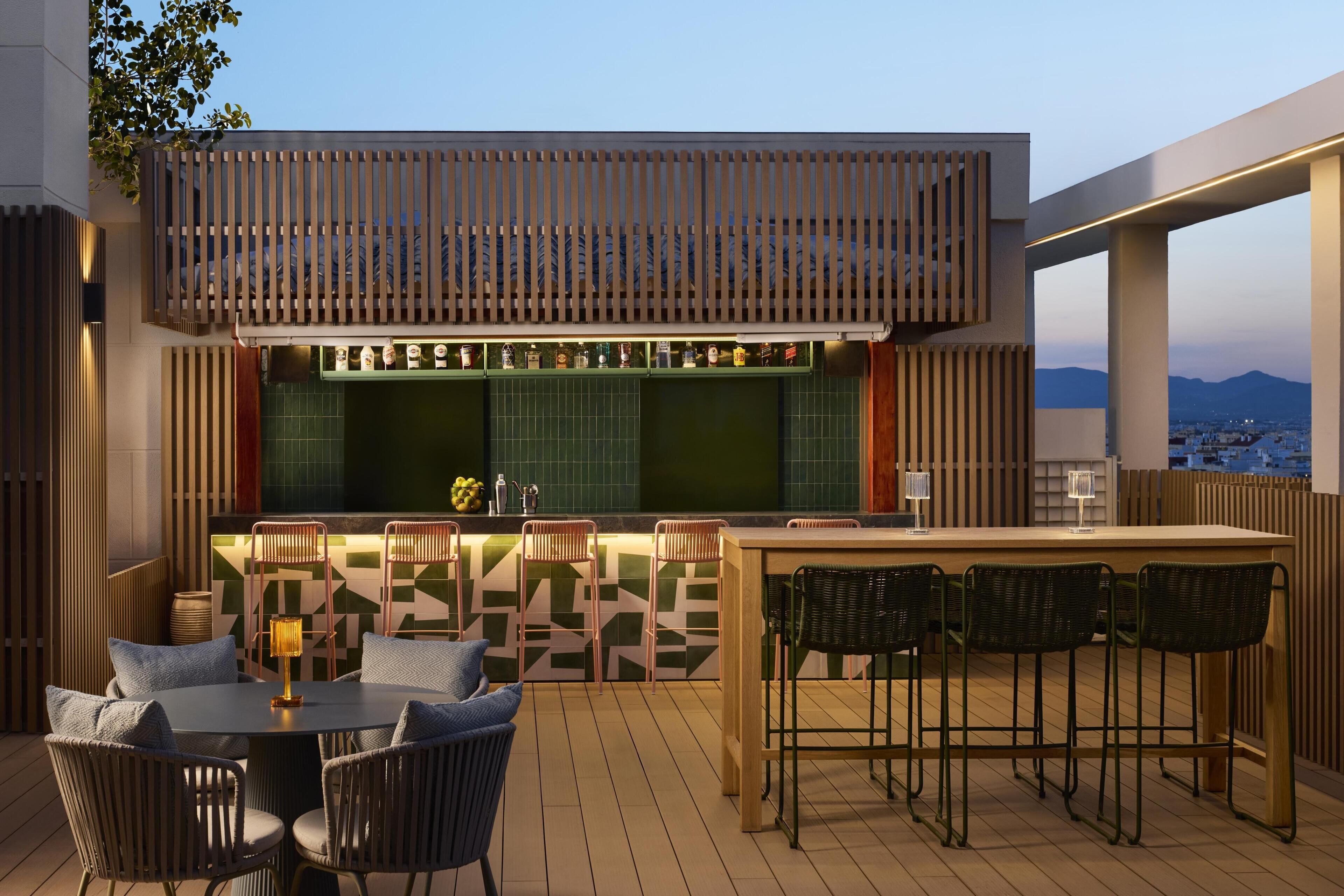 Un área de bar al aire libre con una barra alta, varios taburetes y una mesa redonda con sillas.