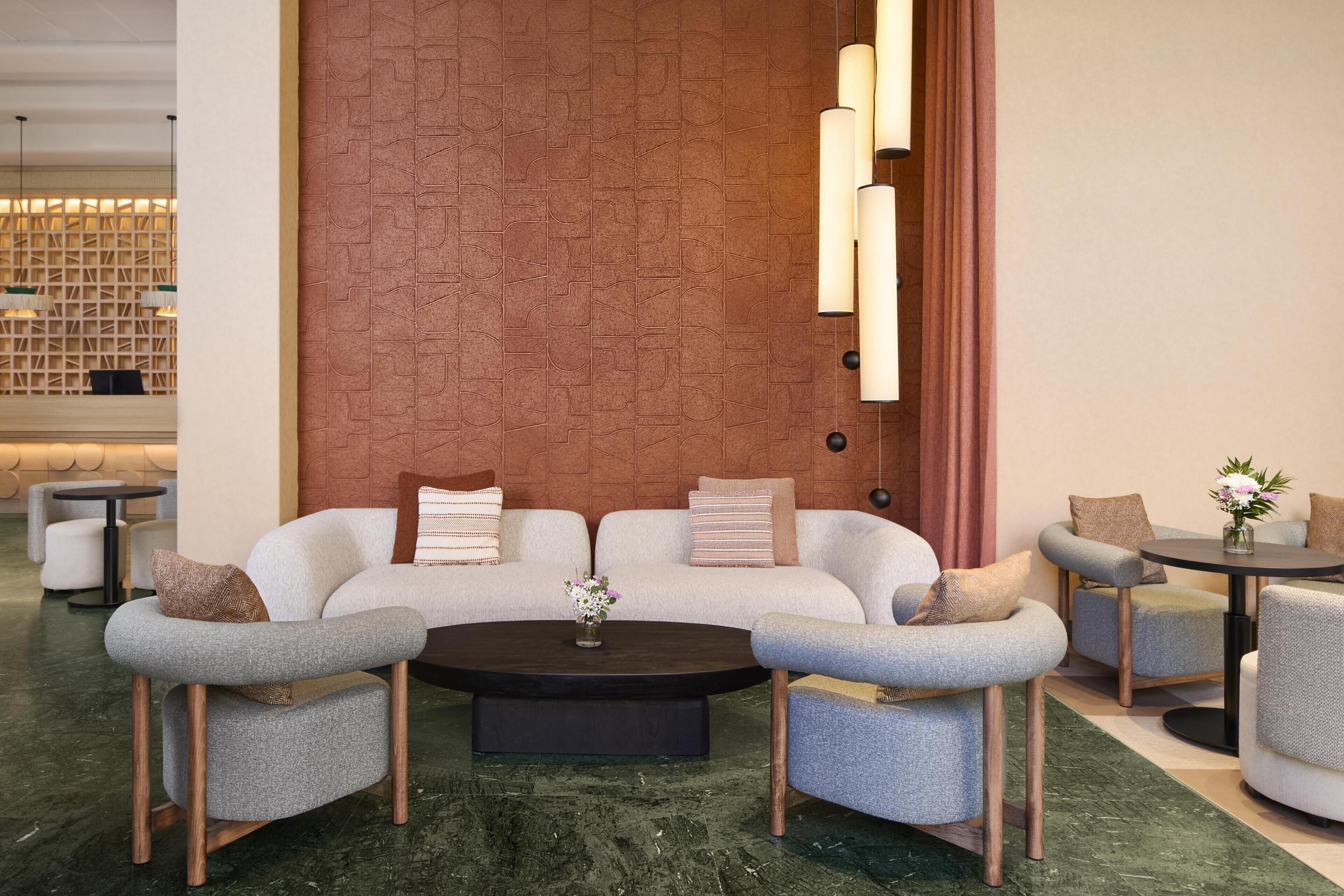 A modern lounge area with a sofa set, armchairs, a coffee table, and a small table with a vase of flowers.