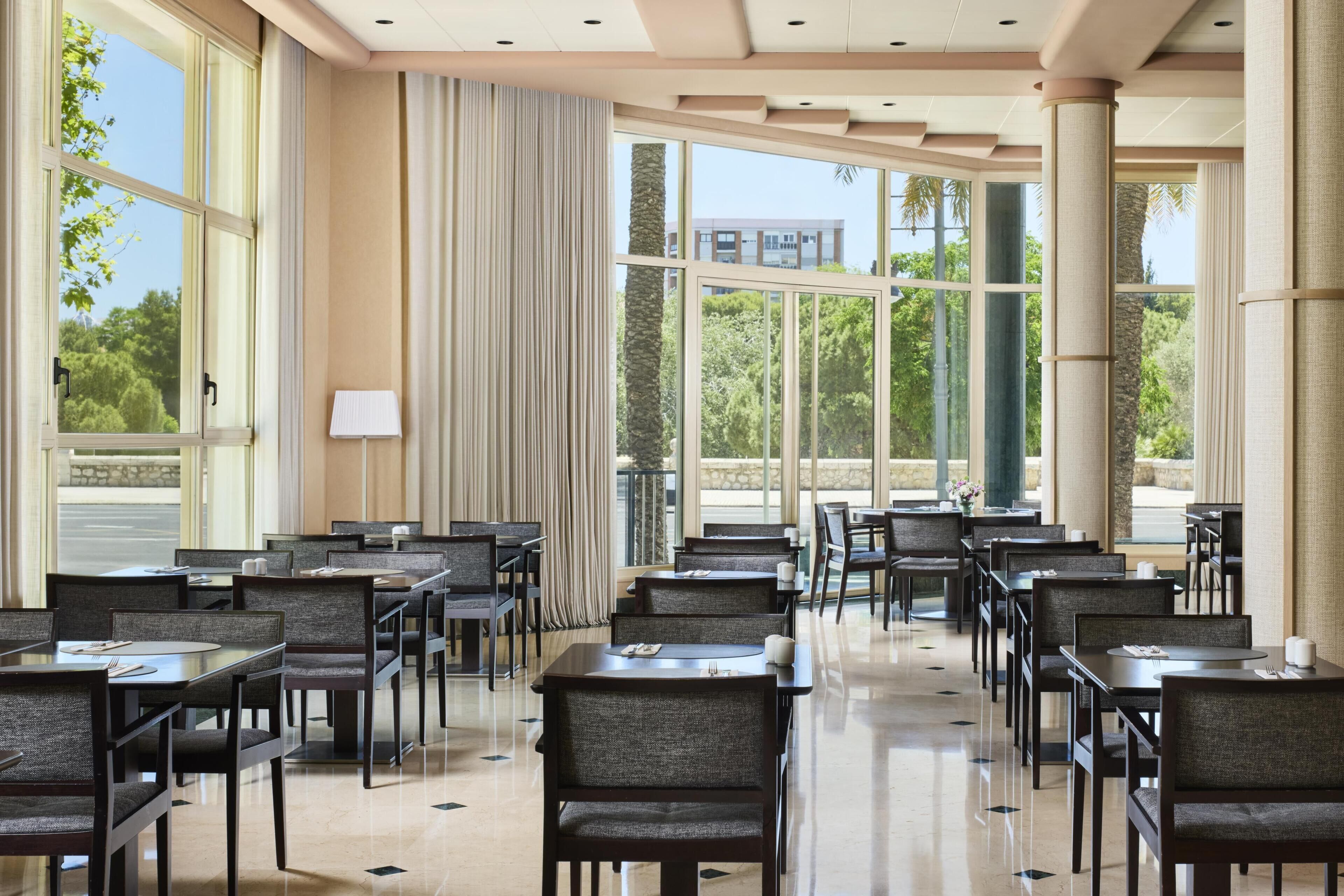 A spacious dining area with multiple tables and chairs, large windows with curtains, and a clean, polished floor.