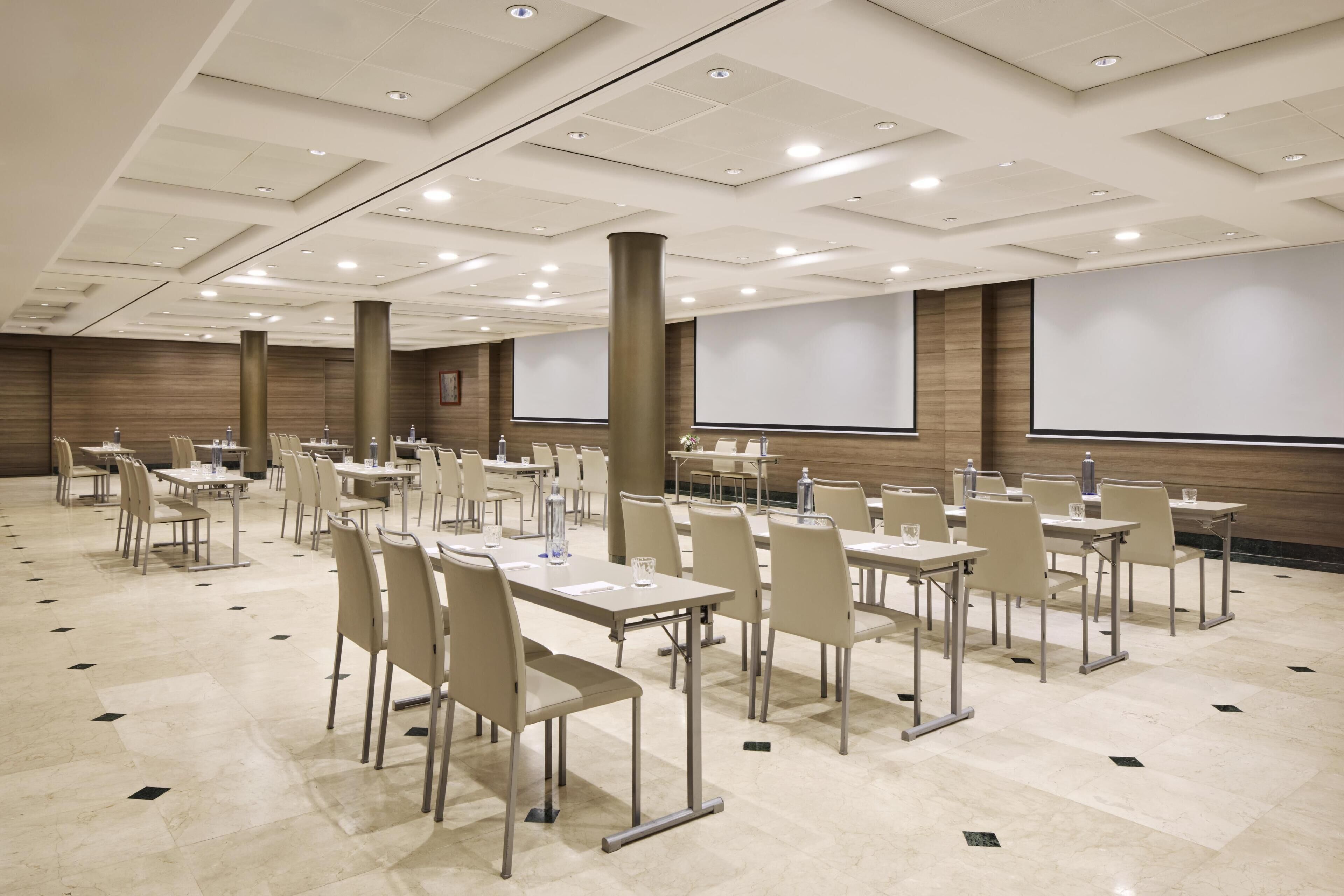 Un salón de conferencias con varias mesas, sillas y una pantalla grande.