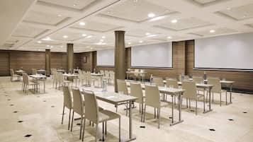 Un salón de conferencias con varias mesas, sillas y una pantalla grande.