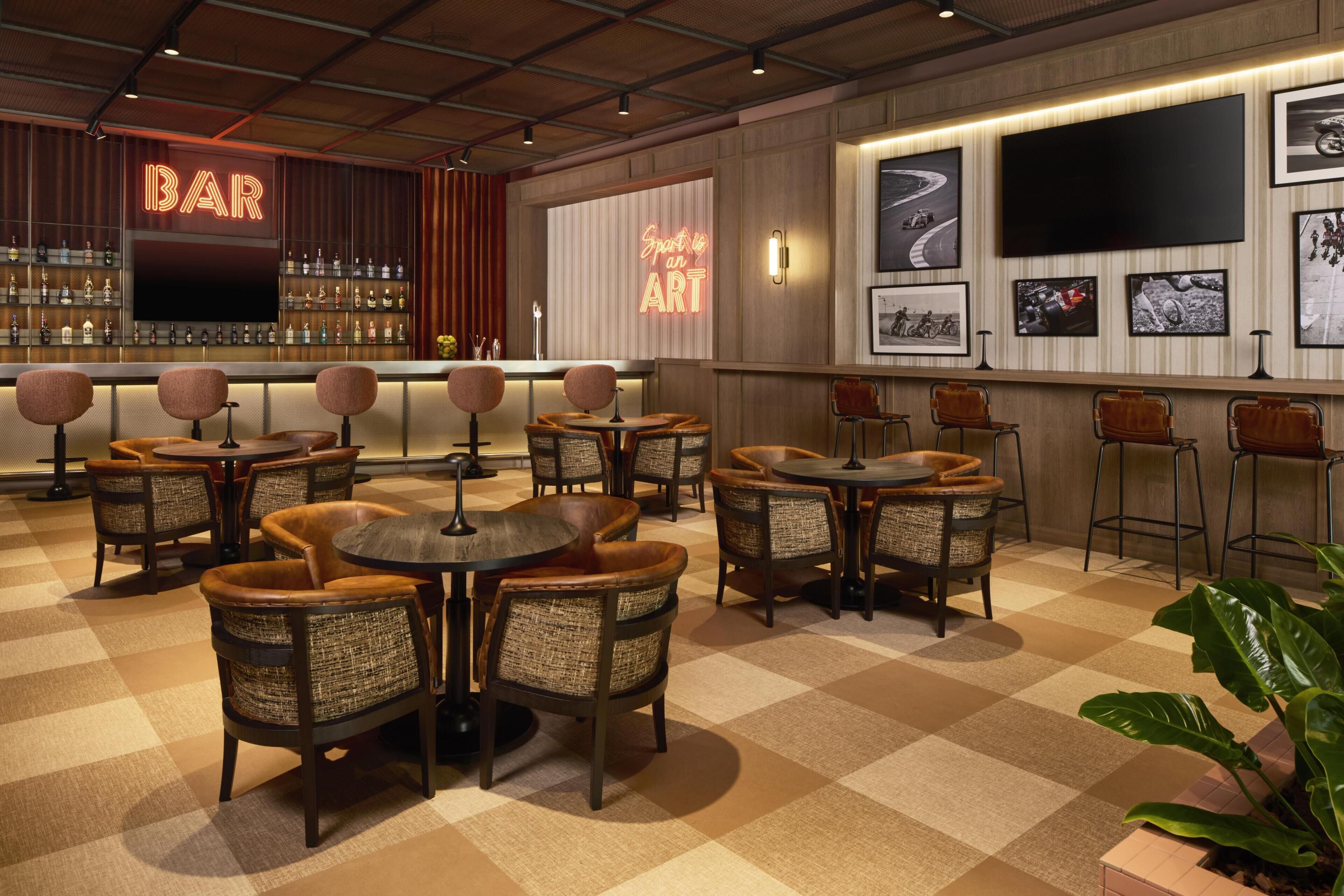 A bar area with a neon sign, multiple seating arrangements, and a wall-mounted TV.