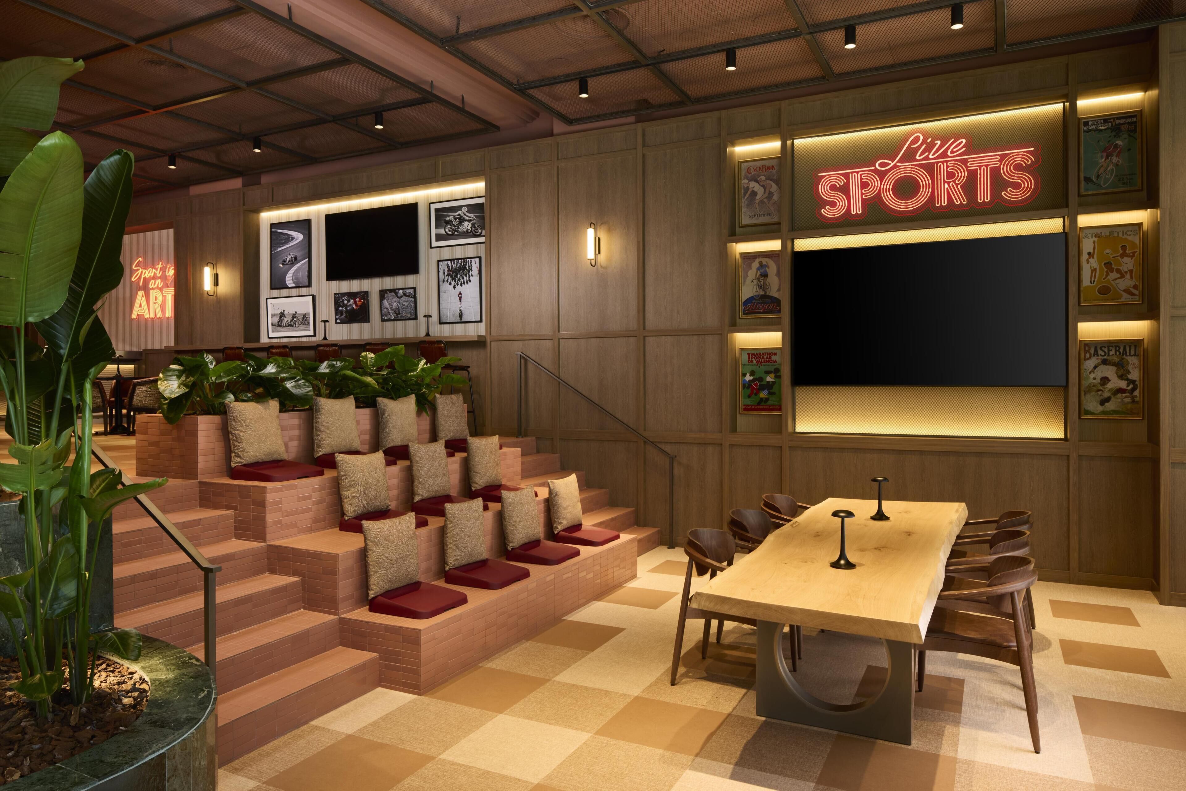 A sports-themed lounge with a checkered floor, a wooden table, and a neon sign reading 'Live SPORTS'.