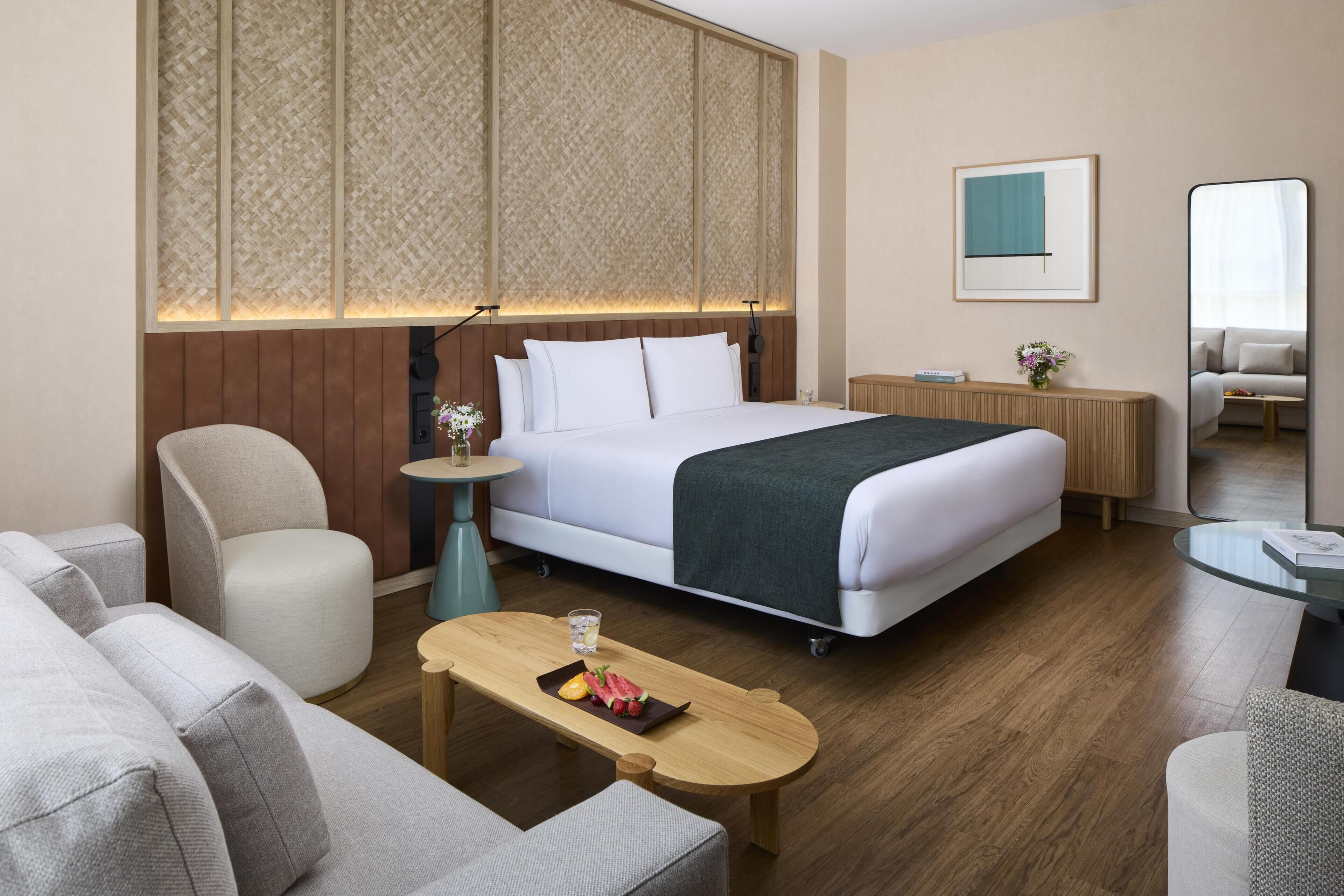 A hotel room with a bed, a seating area with a table, a small side table, and a large mirror.