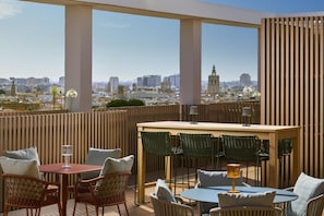 Une terrasse sur le toit offrant une vue sur la ville, avec une table en bois, des chaises en osier et une petite lampe.