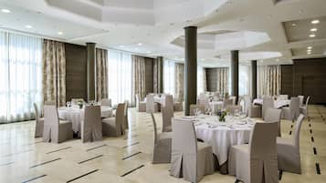 Un amplio salón de banquetes con mesas redondas, sillas color beige y un alto techo con iluminación empotrada.