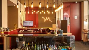 A bar area with a glass display case filled with bottles, a computer monitor, and hanging pendant lights. - Mercure Barcelona Condor (Barcelona)
