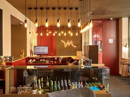 Un espace bar doté d'une vitrine où sont exposées des bouteilles, d'un écran d'ordinateur et de luminaires suspendus.