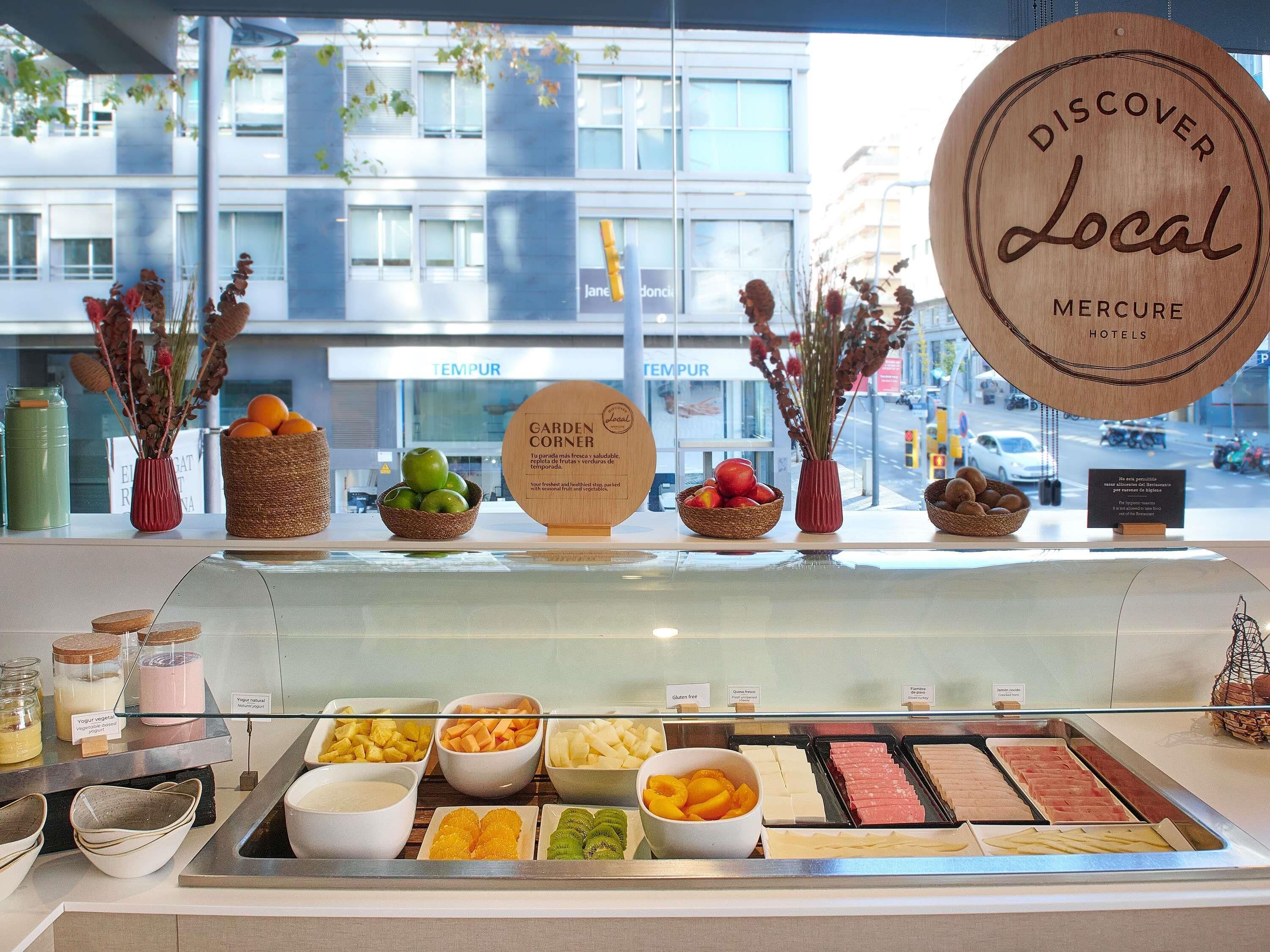 Un présentoir d’hôtel avec des fruits frais, une pancarte indiquant « Coin du jardin » et une autre pancarte indiquant « Découvrez les produits locaux ».
