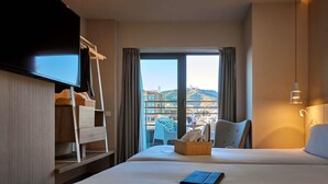 A hotel room with a bed, a TV, a desk, a chair, and a view of the city. - Mercure Barcelona Condor (Barcelona)