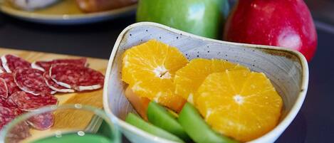 A bowl of sliced oranges and green beans, a plate with sliced salami, and a green apple on a table.