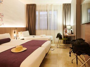 Habitación de hotel con dos camas, un escritorio, una silla, un sombrero, una mochila y una lámpara.