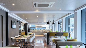 A modern restaurant with a long counter, multiple seating areas, and a kitchen in the background. - Mercure Barcelona Condor (Barcelona)