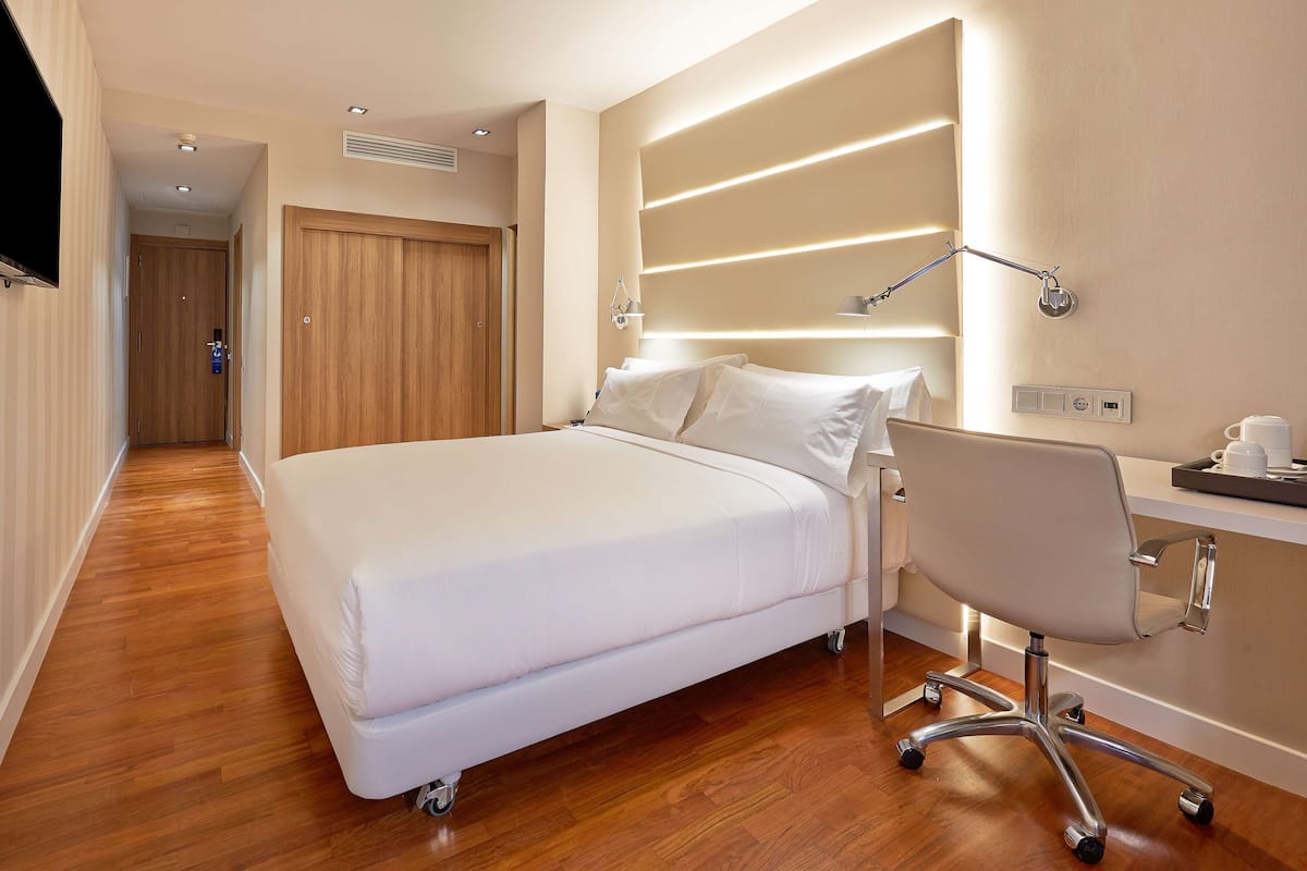 Una habitación de hotel con una cama grande, un escritorio con silla y un televisor.