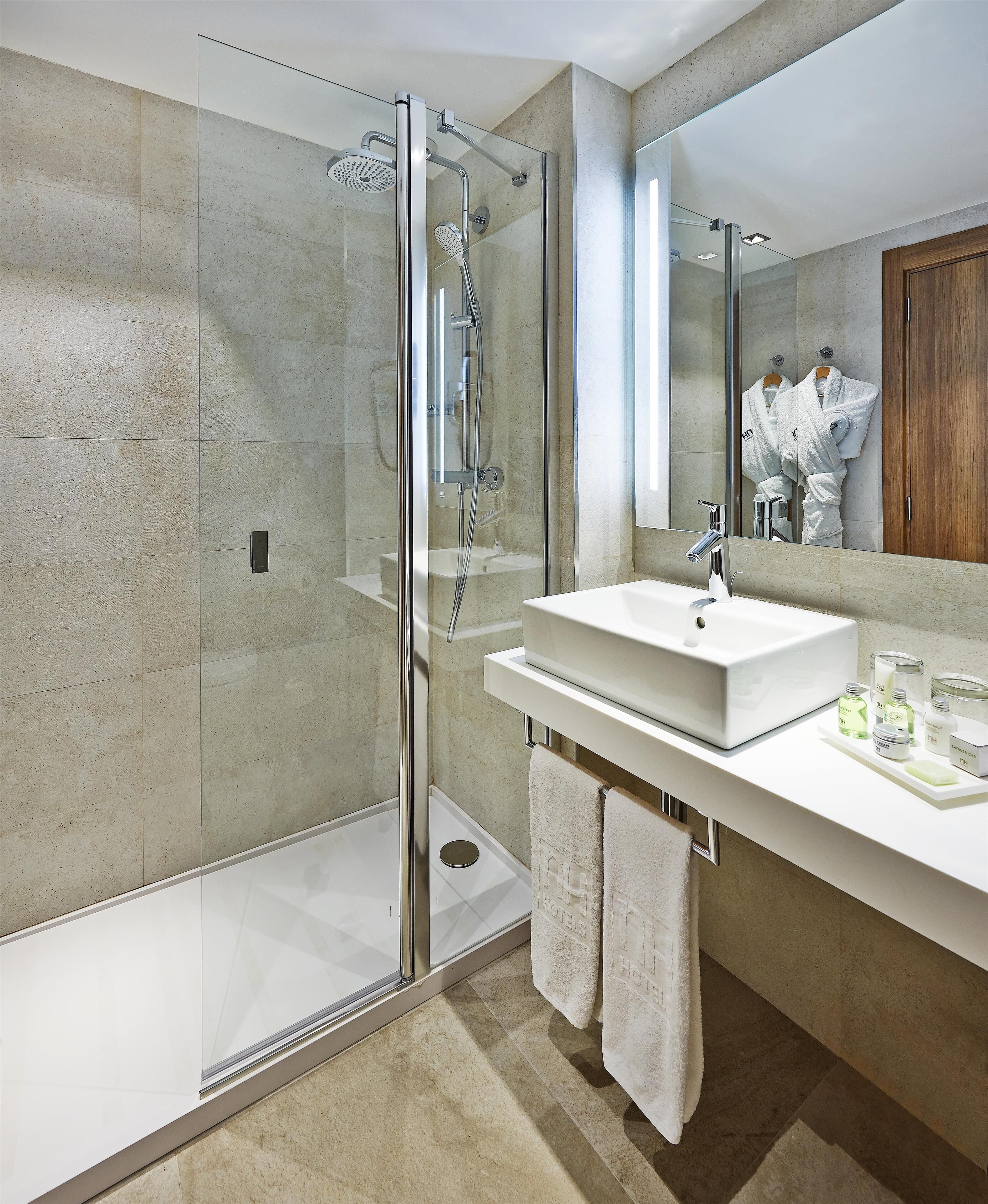 Un baño moderno con cabina de ducha de vidrio, un lavabo blanco y un espejo que refleja un mueble de madera.