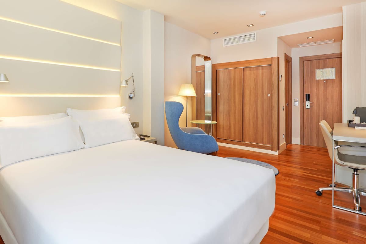Habitación de hotel con una cama grande, lámparas de noche, un escritorio con silla, un armario y un espejo.