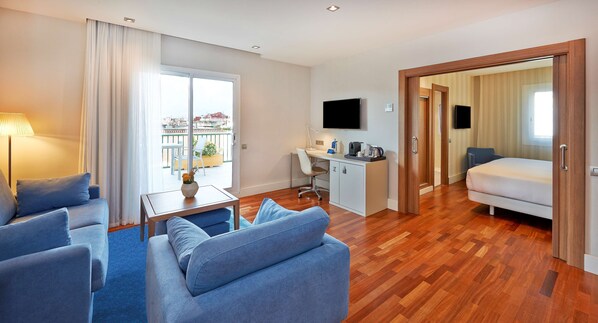 A modern hotel room with a living area, a desk, a bed, and a balcony with a city view. - NH Barcelona Les Corts (Barcelona)