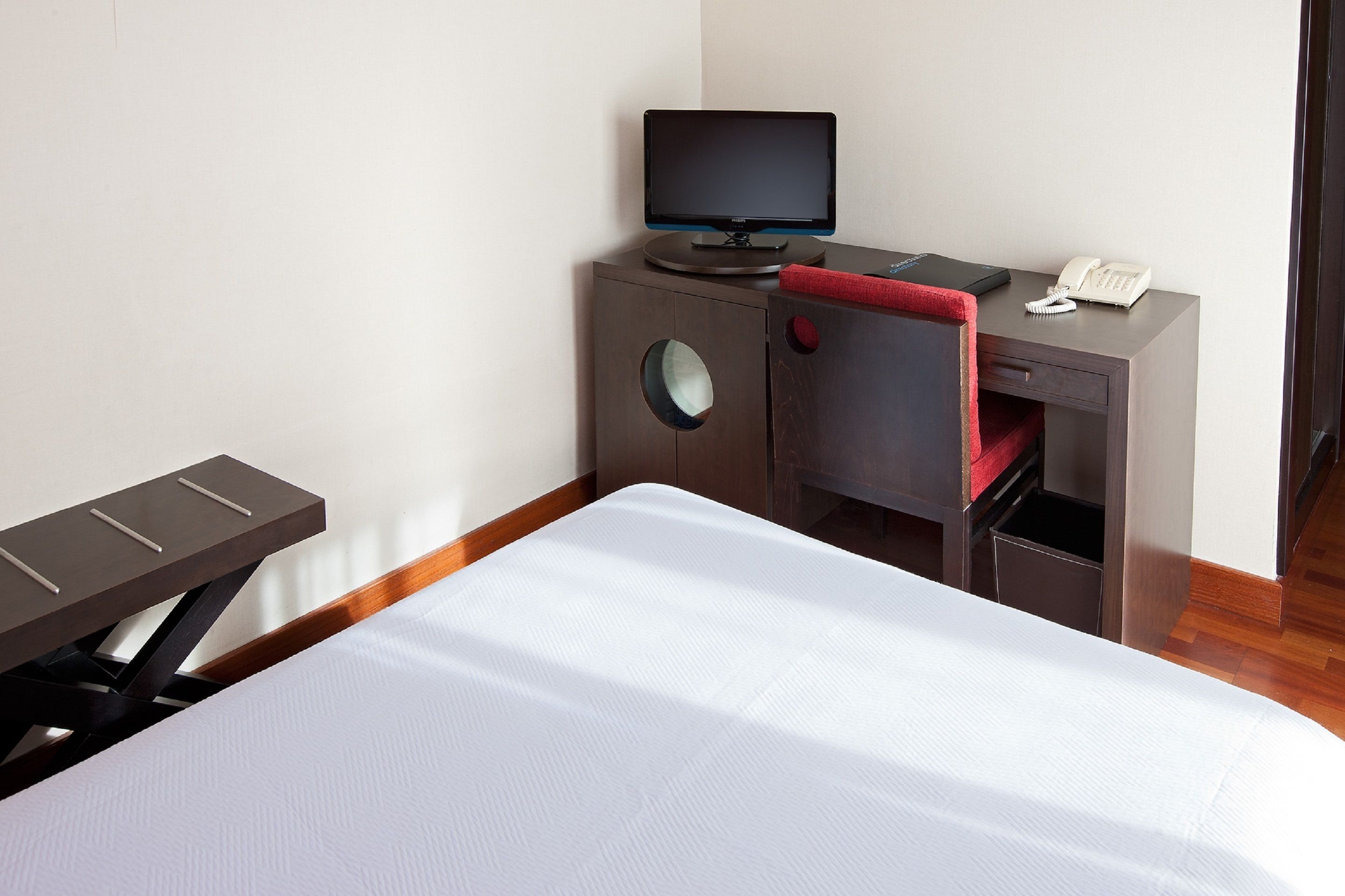 A hotel room with a bed, a desk with a computer, a telephone, and a chair.