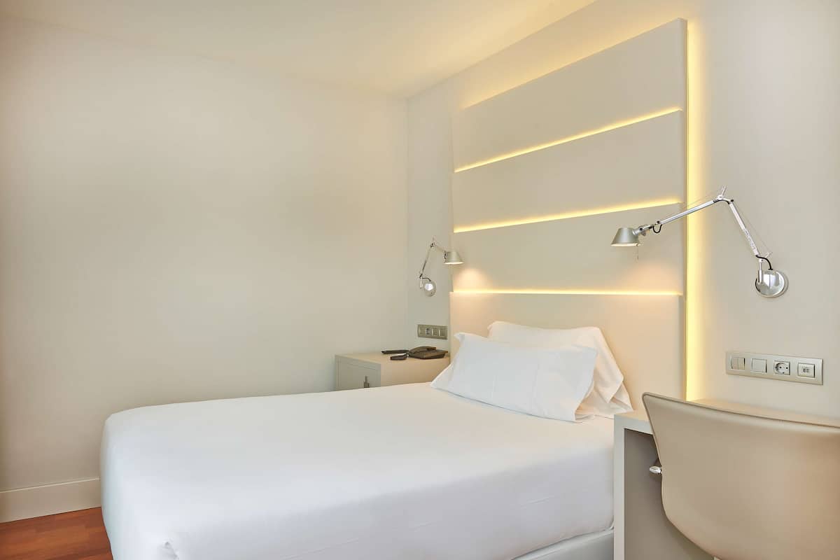 Una habitación de hotel moderna con una cama bien hecha, lámparas de noche y una mesita de noche con un teléfono y una lámpara.