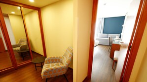 A hotel room with a wooden floor, a patterned armchair, a small table, and a mirror.