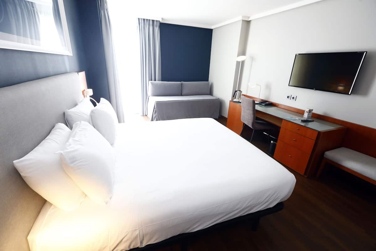 A hotel room with a large bed, a desk, a chair, a television, and a window with curtains.