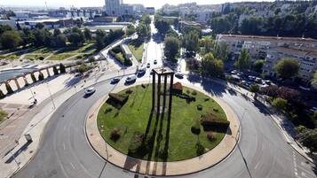 Una glorieta con un monumento central rodeado de follaje y una carretera que lleva a un paisaje urbano con edificios y árboles.