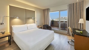 A hotel room with a large bed, bedside tables, a desk with a lamp, a chair, and a view of the city through the window. - NH Ciutat de Reus (Reus)