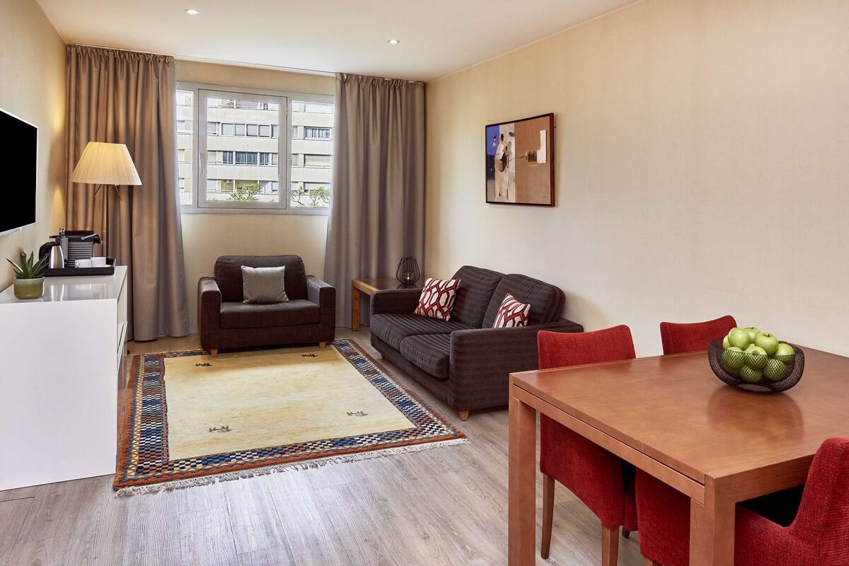 A modern living room with a sofa, a wooden dining table, and a coffee station.
