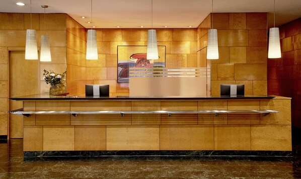 A reception desk with a marble floor, wooden paneling, and pendant lights.