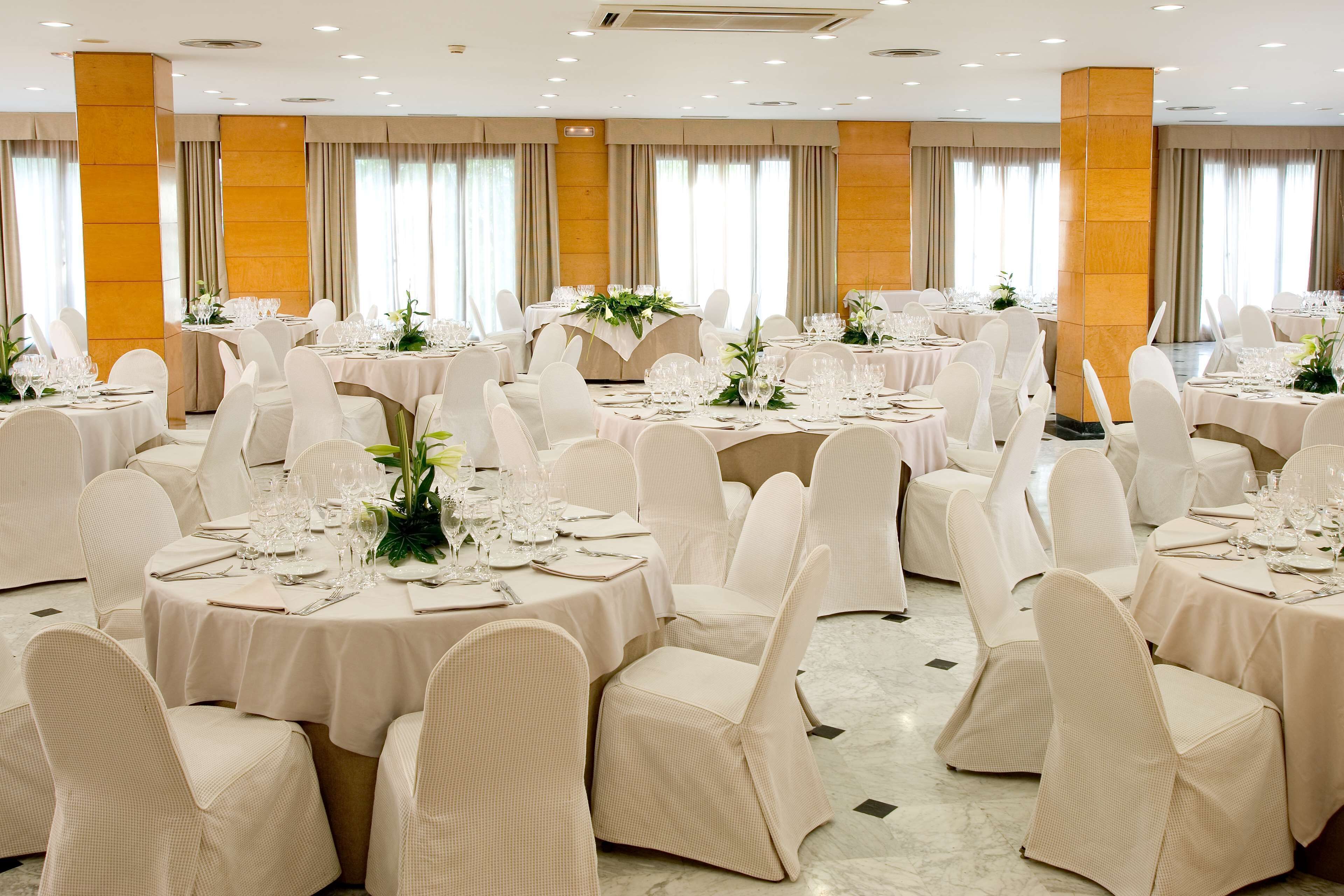 Een balzaal met ronde tafels, witte stoelen en bloemdecoraties.