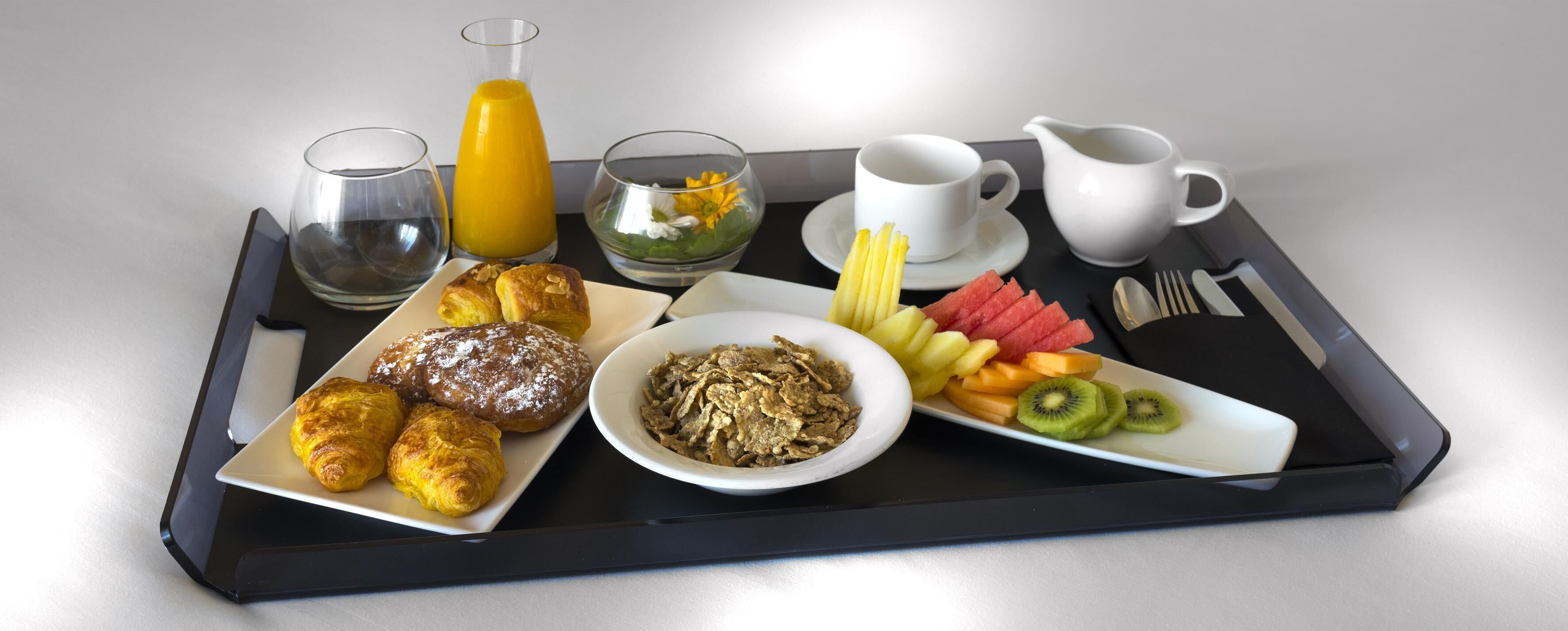 Een dienblad met ontbijtartikelen zoals croissants, cornflakes, fruit en drankjes.