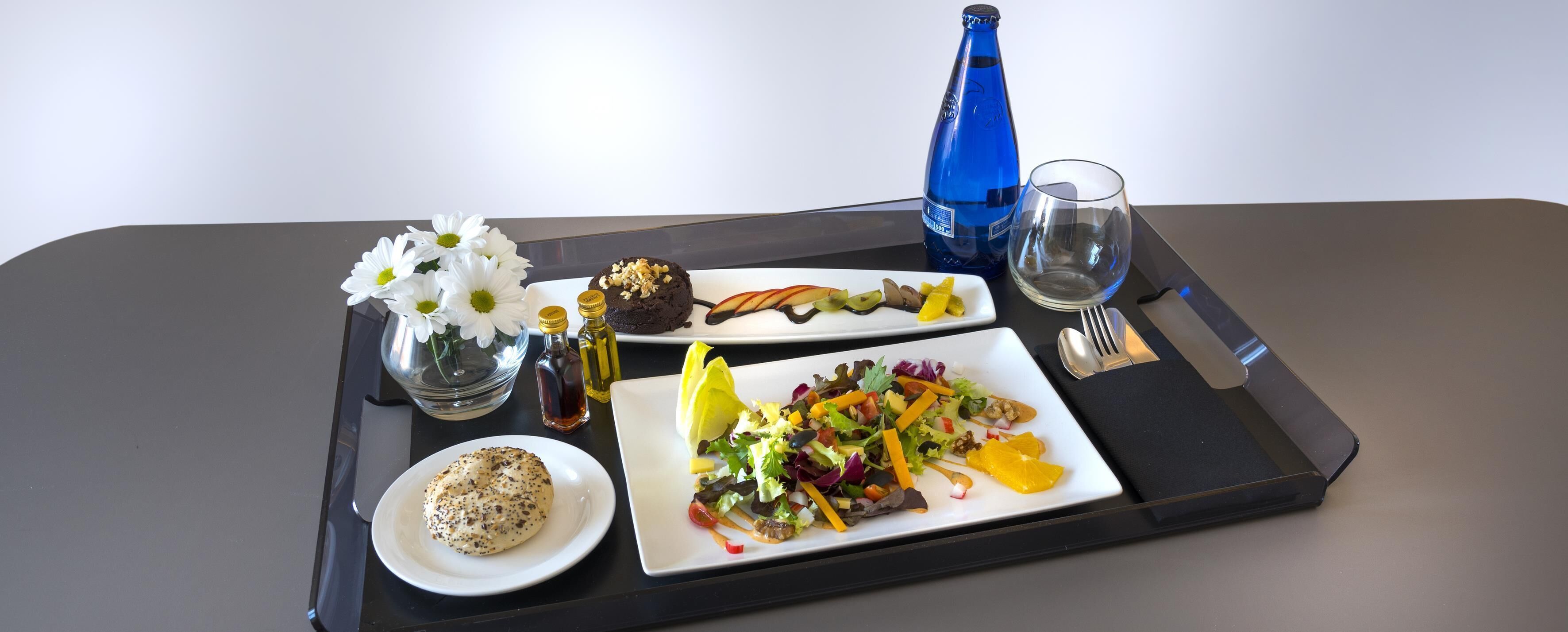 Un plateau contenant divers aliments, notamment un bagel, un muffin, une salade et un dessert, ainsi qu’une bouteille d’eau et un verre.