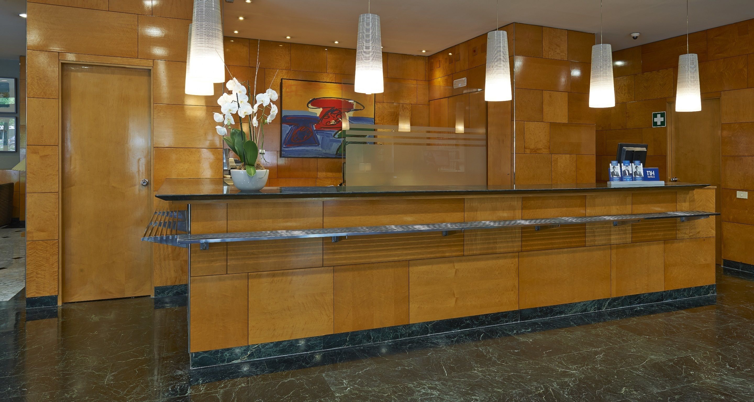 Un mostrador de recepción con encimera de mármol, paneles de madera e iluminación colgante.