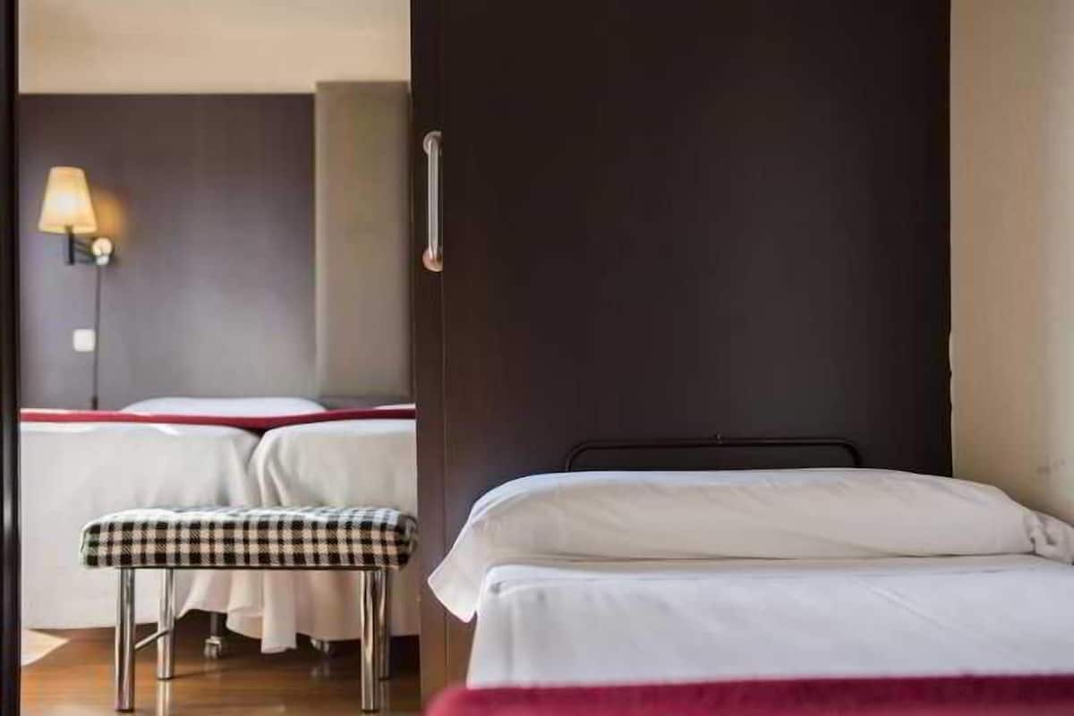 Une chambre d’hôtel avec un lit, un banc et une lampe fixée au mur.