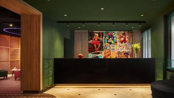A modern reception area with a dark reception desk, green walls, and a colorful mural.