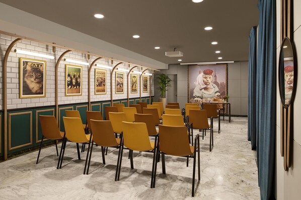 A conference room with rows of yellow chairs, a white tiled wall with framed posters, and a large mural on the back wall.
