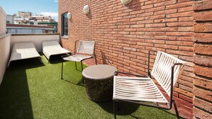 A rooftop terrace with a brick wall, two lounge chairs, a round table, and two wall-mounted lights. - Bohemian Entenza (Barcelona)